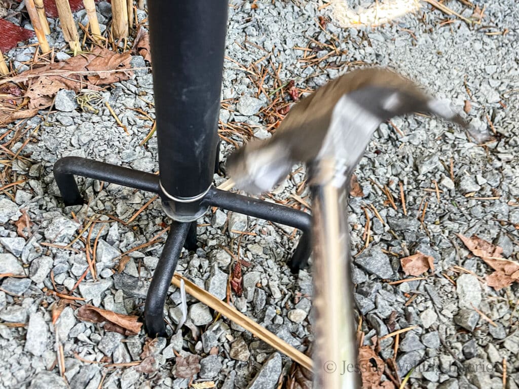 hammer pounding the base of a fork-style string light pole into the ground