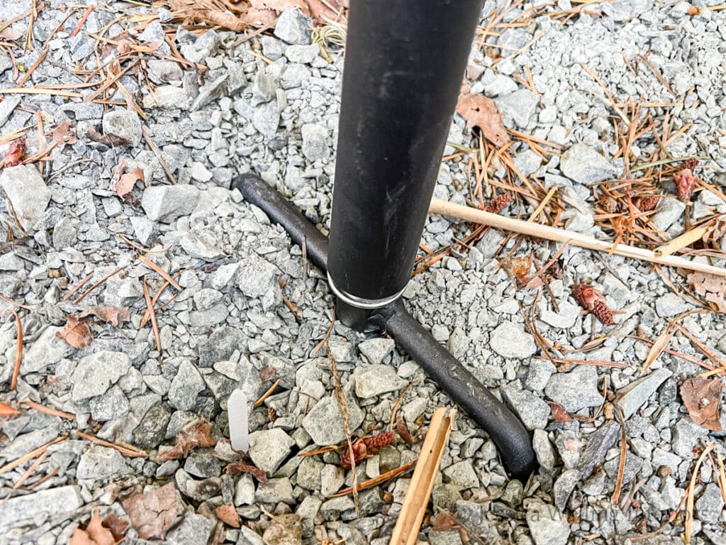 close-up of the base of a fork-style string light pole installed on a gravel patio