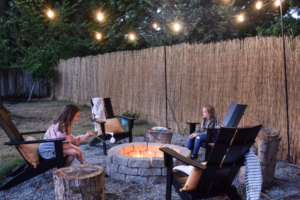 low light photo of two girls roasting marshmallows over a DIY fire pit