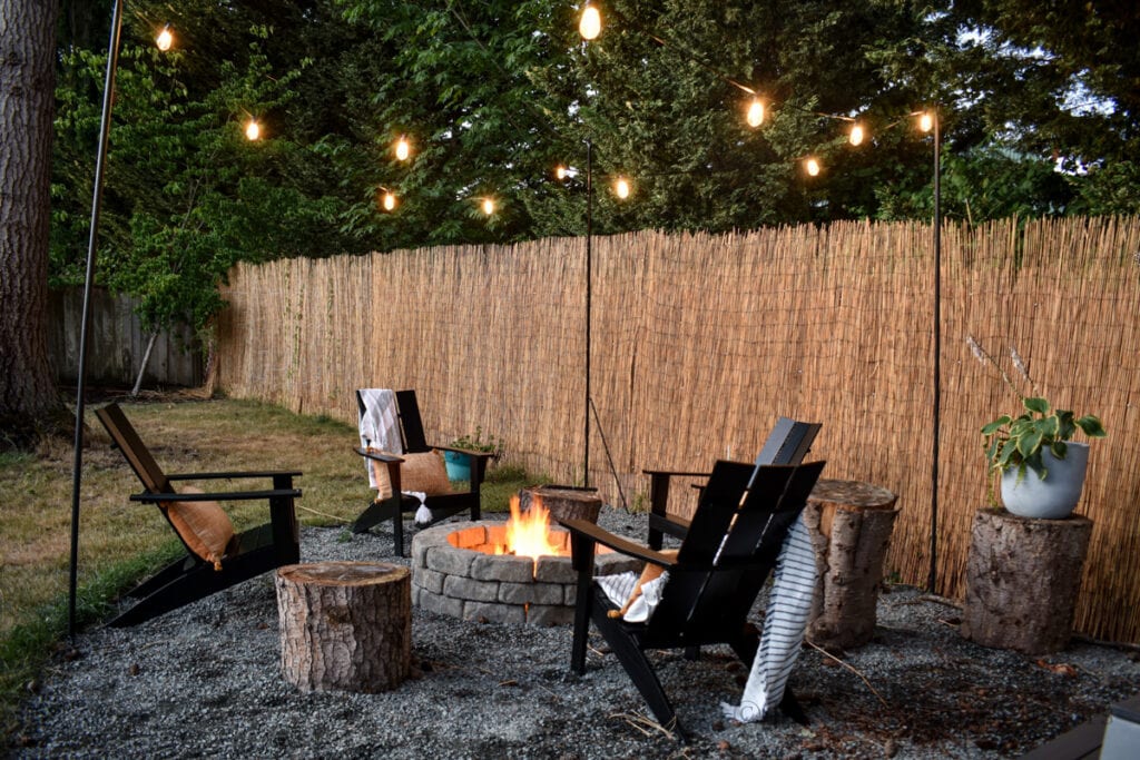 night time photo of fire pit surrounded by chairs and string light poles hung with glowing string lights