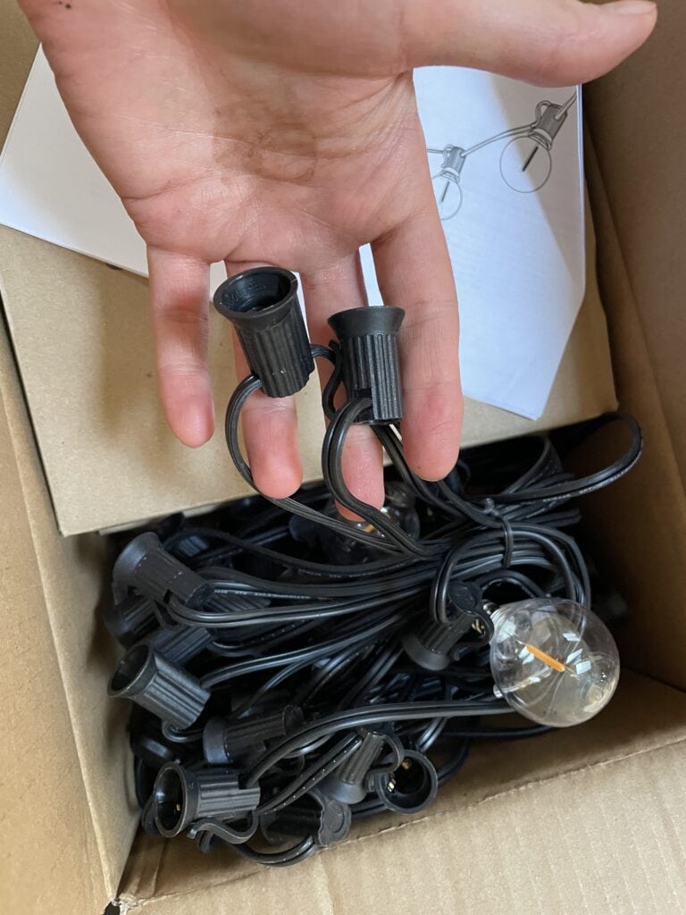 open box of LED string lights with hand holding up two of the sockets