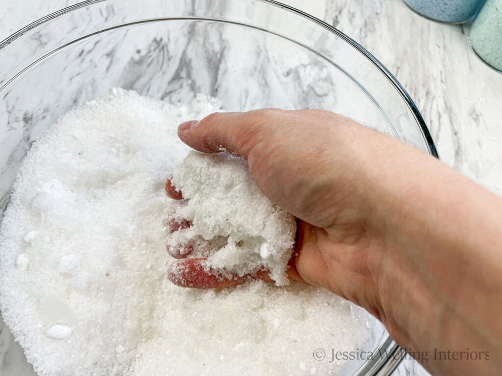 hand in a mixing bowl sifting DIY bath salts to combine them