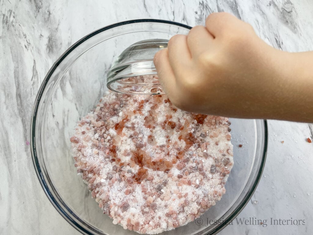 small bowl of oils being poured into a bowl of bath salt mixture