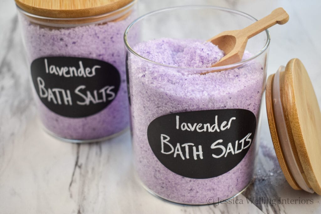 two jars of homemade lavender bath salts with a wood scoop