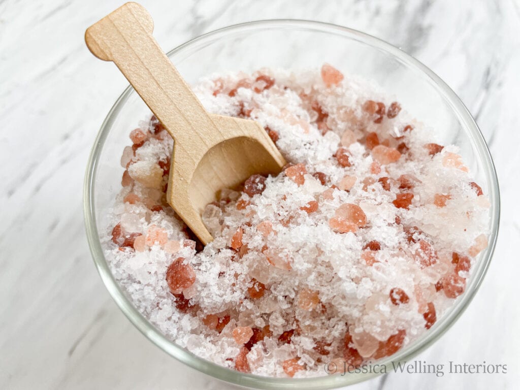 overhead view of a glass jar of pink Himalayan bath salt with a wood scoop
