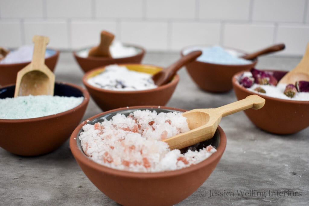 several bowls of DIY bath salts with wood scoops on a countertop
