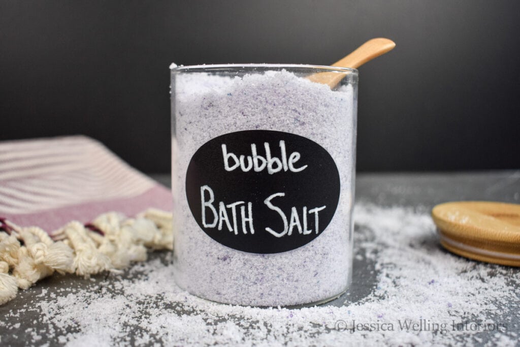 jar of bubble bath salt on a countertop with a wood scoop sticking out the top