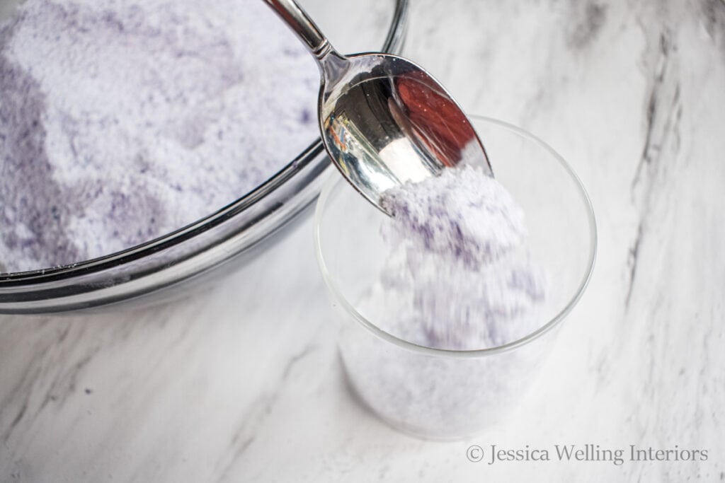 purple bath salts being spooned into a glass jar for storage