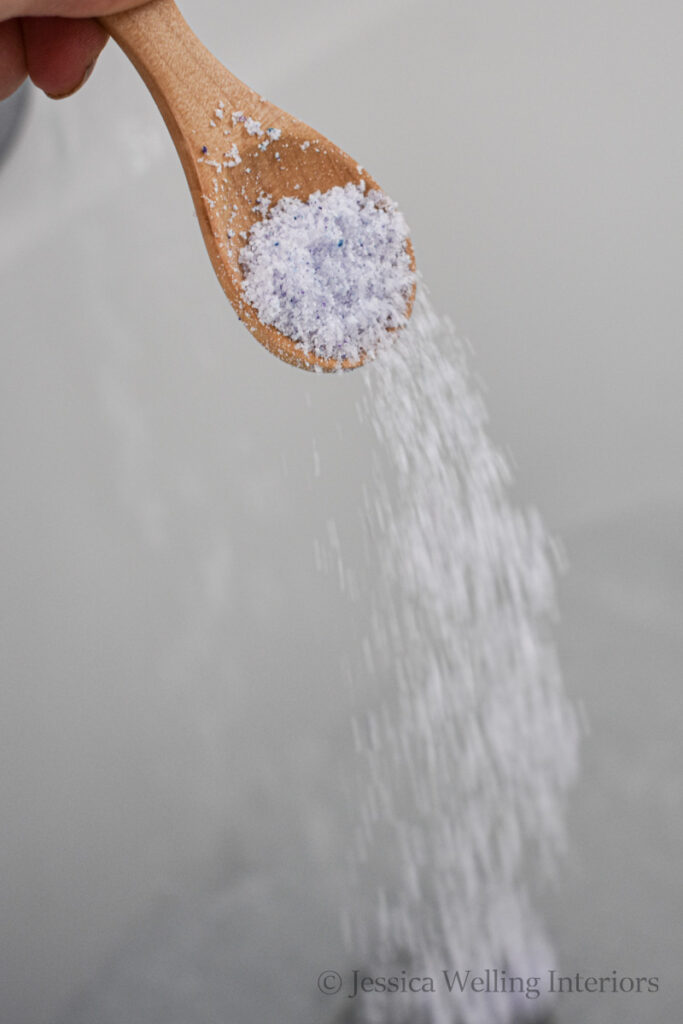 bubbling bath salts being poured into a bath from a wood scoop