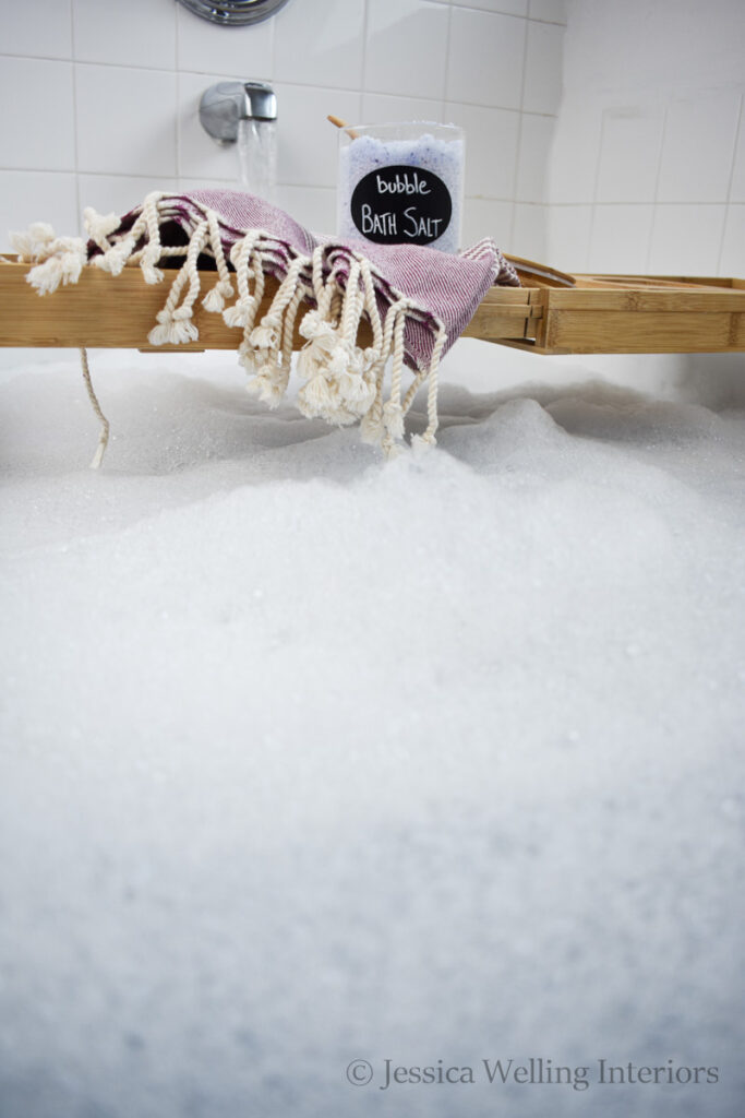 jar of bubble bath salt sitting on a wood bath tray over a tub full of bubble bath