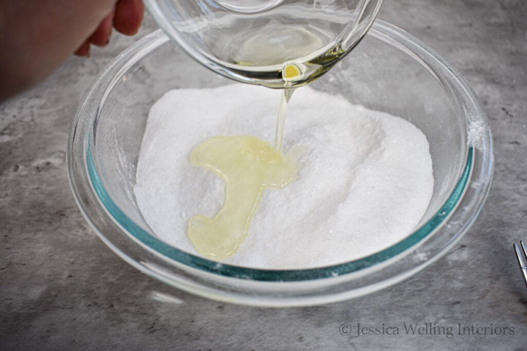 oil mixture being added to a bowl of salt mixture to make bath salts
