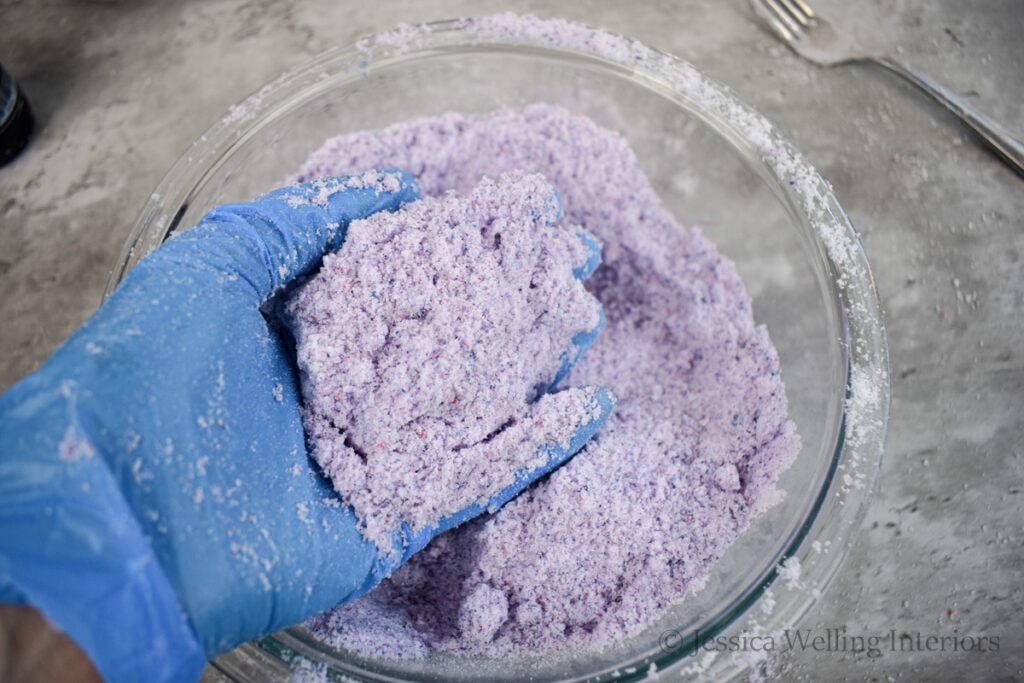 gloved hand mixing color into fizzing bath salts