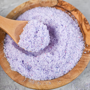 wood bowl of purple fizzy bath salt with a wood scoop
