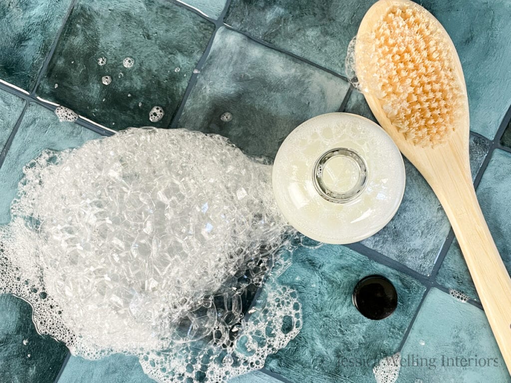 overhead view of a bottle of homemade bubble bath next to a pile of bubbles and a shower brush