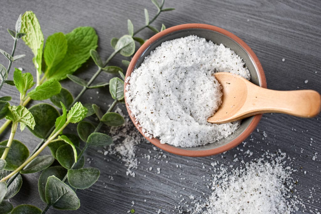 bowl of homemade peppermint foot soak on a table with eucalyptus and peppermint sprigs