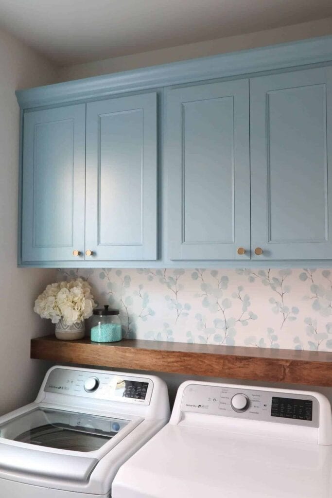 pretty laundry room with wallpaper and blue painted cabinets