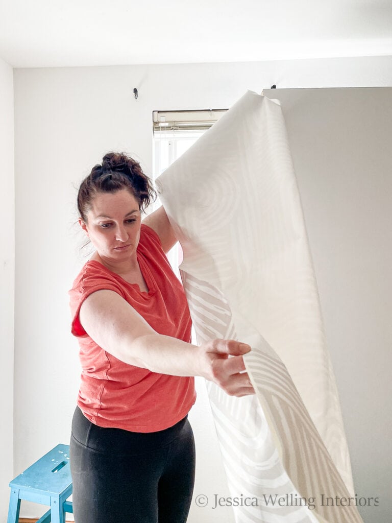 woman holding up a strip of wallpaper before installing it