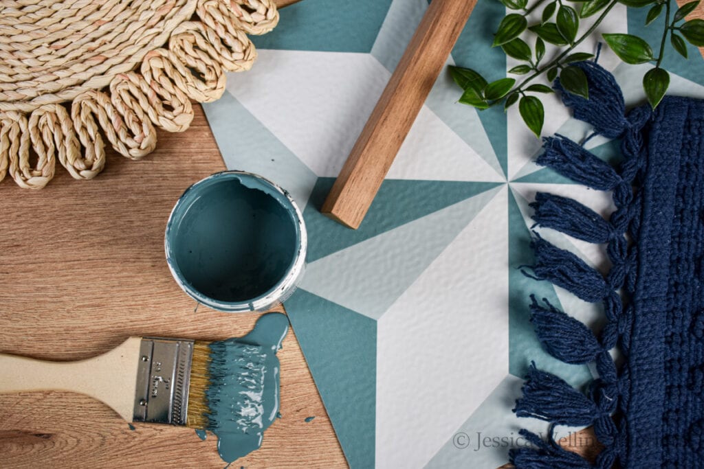 flat lay photo of floor tile, an open can of teal paint with a paintbrush, a cabinet pull, a navy blue rug, etc.