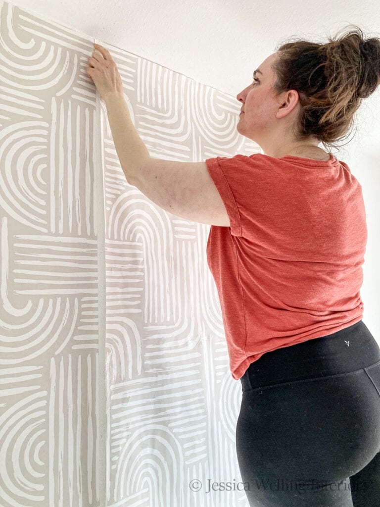 woman lining up a run of wallpaper before hanging it on the wall