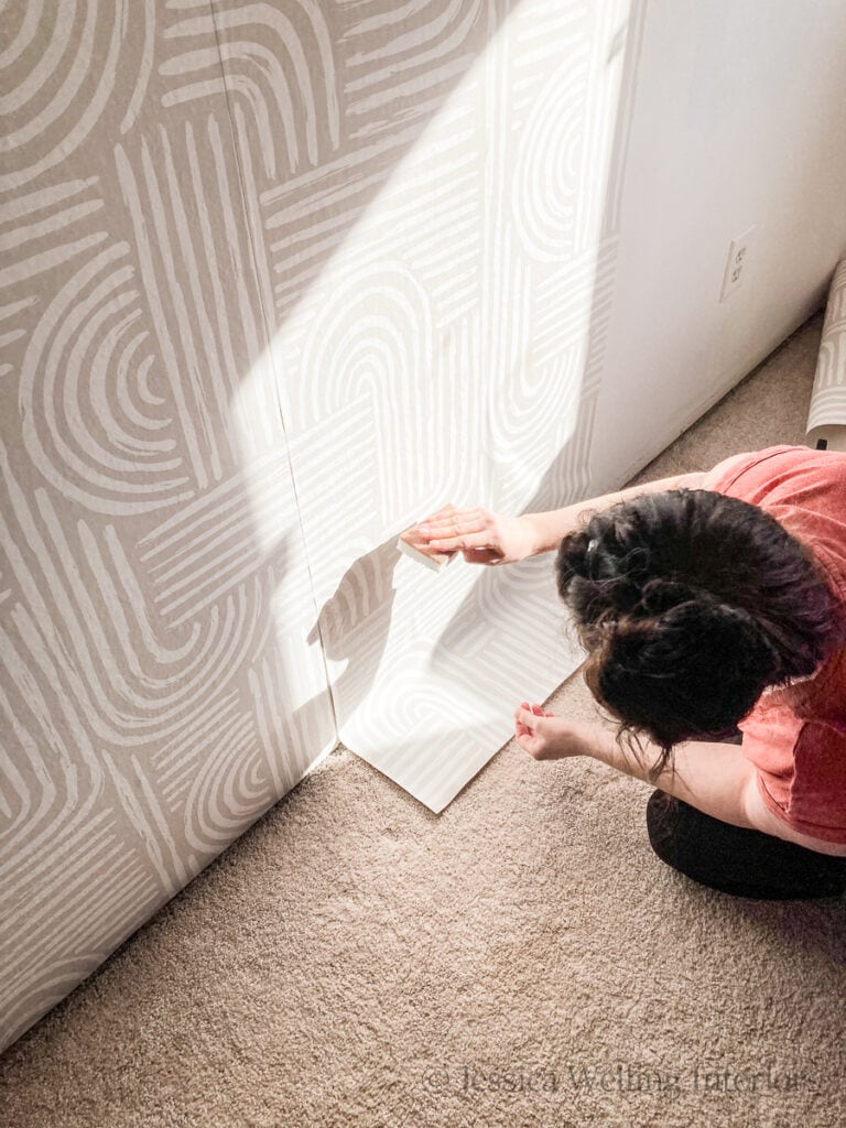 woman smoothing pre-pasted wallpaper with a damp sponge