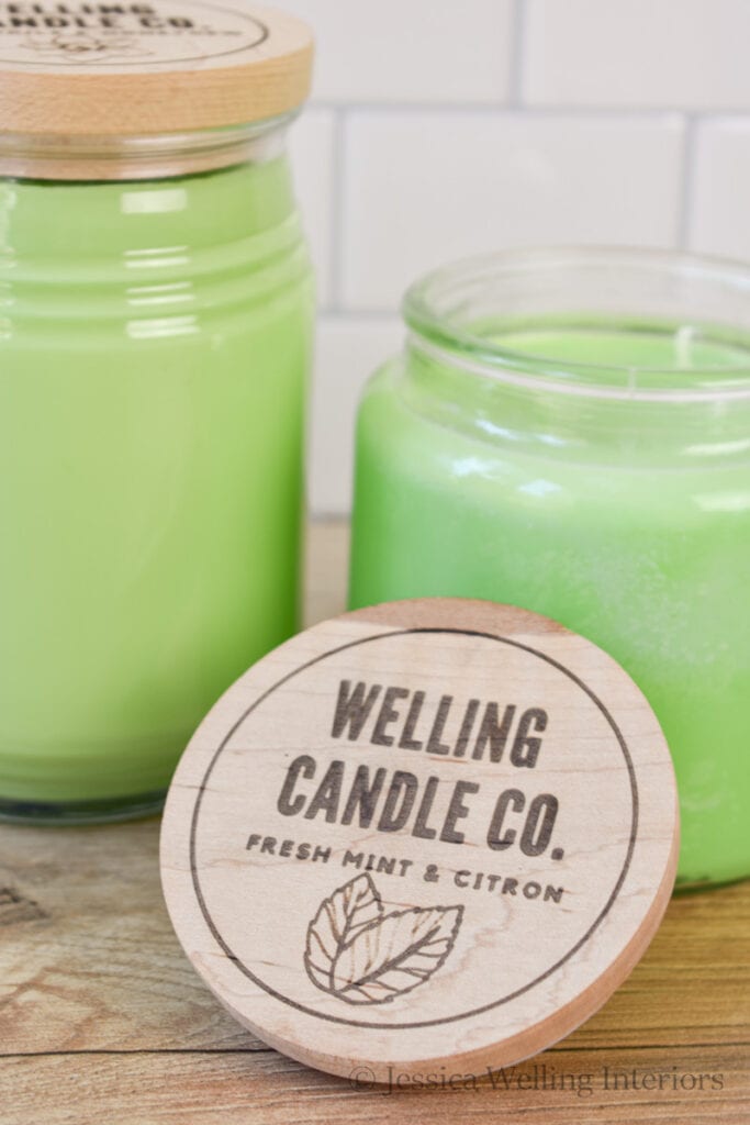 Custom engraved wood candle jar lid in front of two green handmade candles